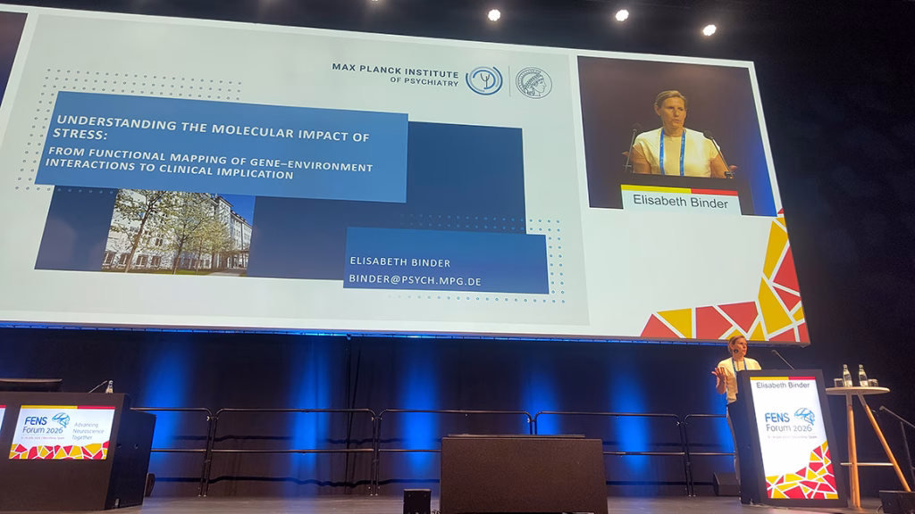 Conference stage with a large presentation slide titled 'Understanding the Molecular Impact of Stress' and a speaker identified as Elisabeth Binder at a podium